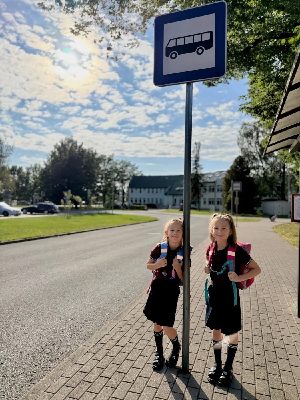 Divas skolnieces ar mugursomām gaida pieturā